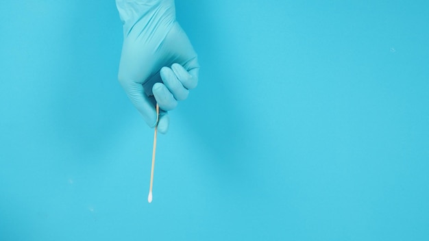 Cotton stick in hand with blue latex glove on blue background