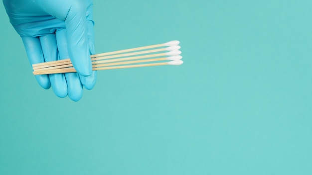 Cotton sticks for swab in hand with blue medical gloves or
latex glove on mint green or tiffany blue background.covid-19
concept