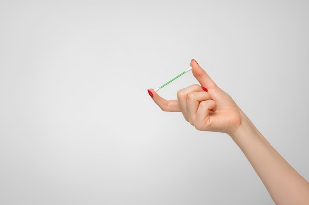 A cotton swab for cleaning the ears in a woman's hand with red nail polish.