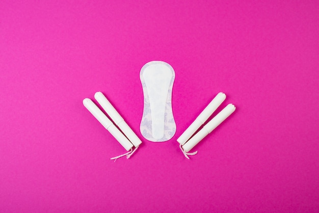 Cotton tampons with an applicator and sanitary pads on a pink background.