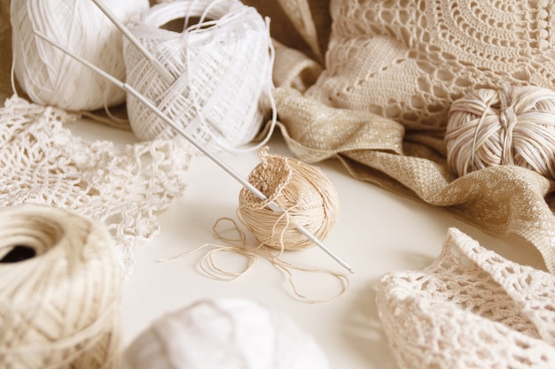 Cotton thread and hook on a table surrounded by beige cotton\
balls and doilies