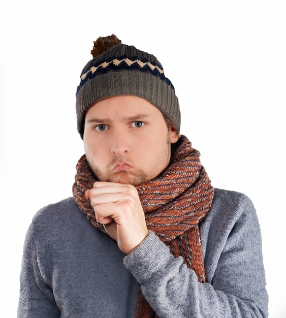 Coughing young ill man wearing winter hat with scarf putting hand on mouth isolated
