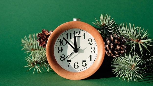 Countdown to midnight wood alarm clock with fir tree and pine\
cones green paper background