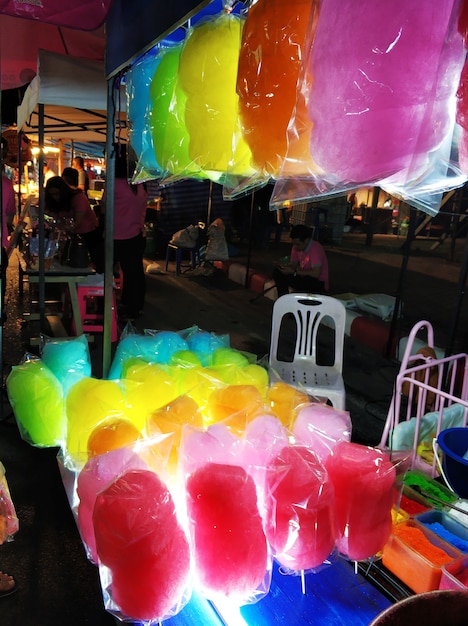 A counter selling colored cotton candy at a nighttime street food market in Asia.