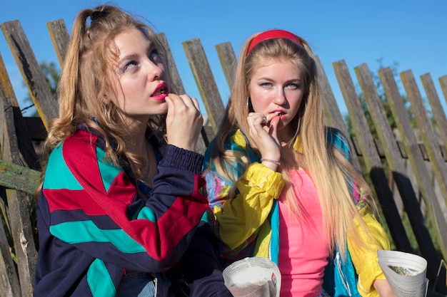 Country girls dressed in the style of the nineties eating sunflower seeds from a paper bag