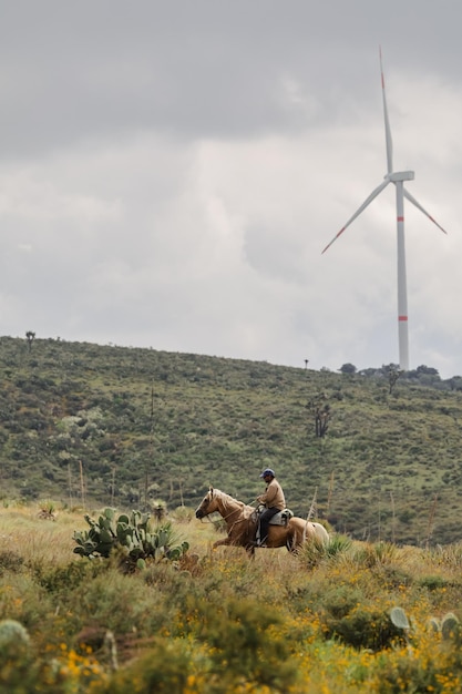 Photo country man on horseback in landscape with wind power generator vertical picture