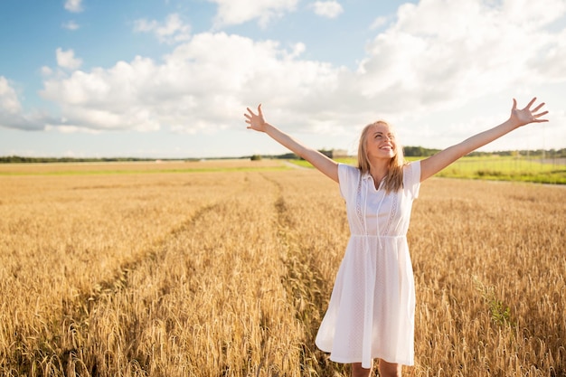 country, nature, summer holidays, vacation and people concept - smiling young woman in white dress on cereal field