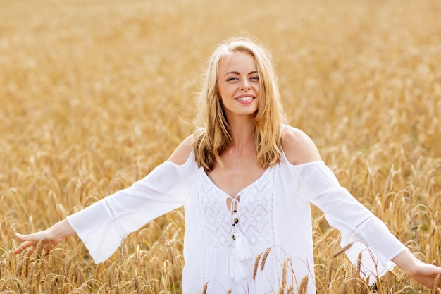 country, nature, summer holidays, vacation and people concept - smiling young woman in white dress on cereal field