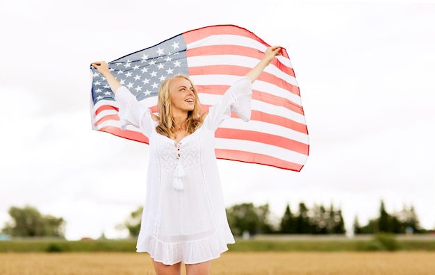 country, patriotism, independence day and people concept - happy smiling young woman in white dress with national american flag on cereal field