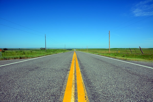 Country road amidst field against blue sky