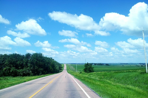 Country road by field against sky