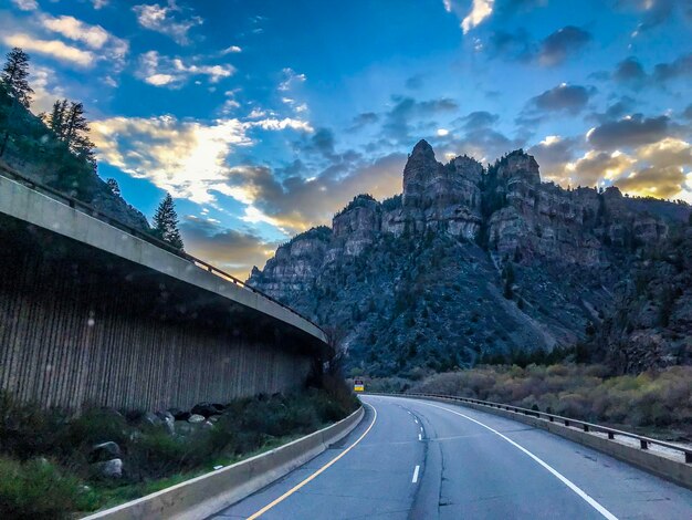 Country road by mountains against sky