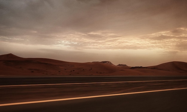 Foto strada di campagna dalle dune di sabbia nel deserto contro il cielo durante il tramonto