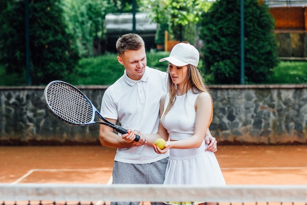 Couple of adult tennis players. Athletic woman and man giving cheerful smiles, holding racquets and wearing uniforms.