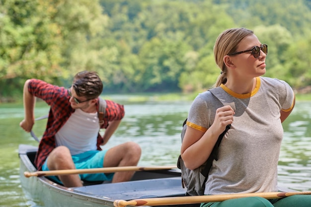 Couple adventurous explorer friends are canoeing in a wild river surrounded by the beautiful nature