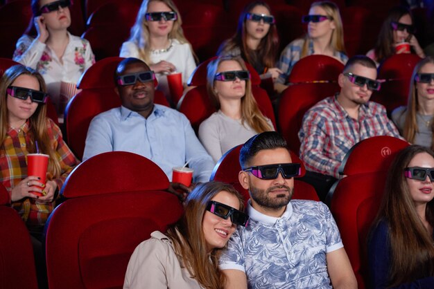 Coppia uomo arabo e donna bruna seduti insieme nel cinema, abbracciando e guardando la commedia.