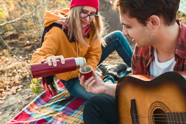 A couple are resting in nature against the background of autumn trees and the river guy plays the