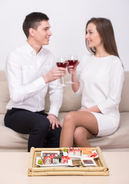 Couple are sitting together, eating sushi and drinking wine.