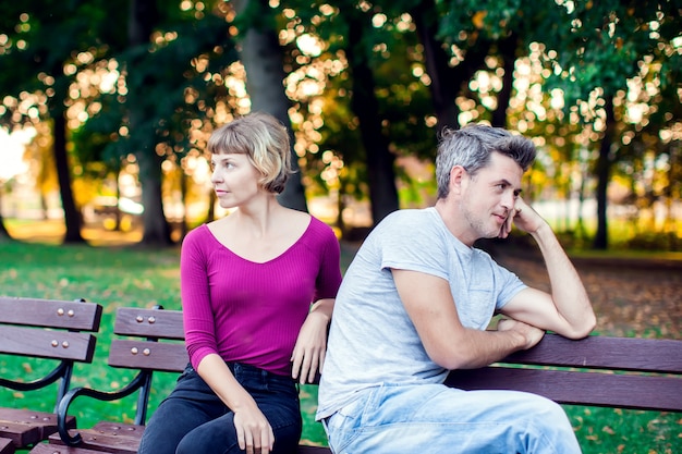 A couple arguing while sitting on bench in park. Problems in relationship.