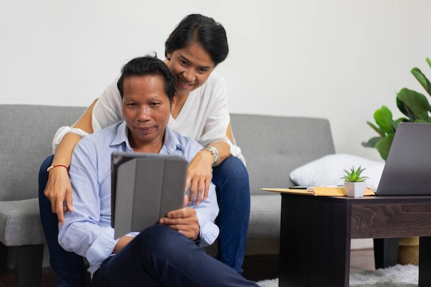 Coppia di genitori asiatici seduti in soggiorno durante l'utilizzo di tablet digitale per videoconferenza