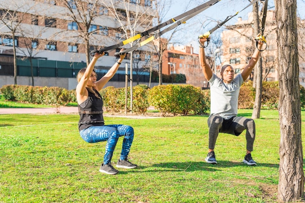 Couple of athletes exercising with trx fitness straps in the park. Adult man and woman exercising outdoors.