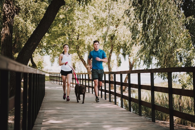 運動選手のカップルは緑豊かな公園で走っています。