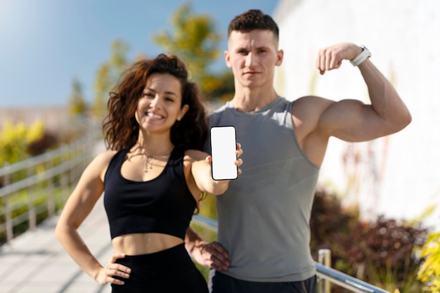 Couple of athletes looking at camera and posing with smartphone while resting