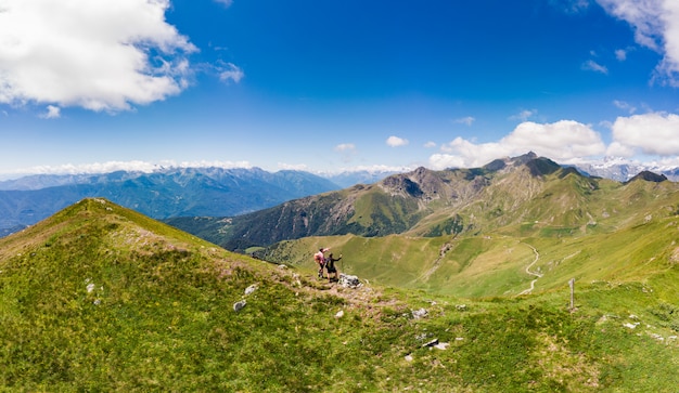 Couple backpackers hiking on mountain top, scenic landscape. Summer adventures on the Alps. Conquering success adult having fun wellbeing fitness