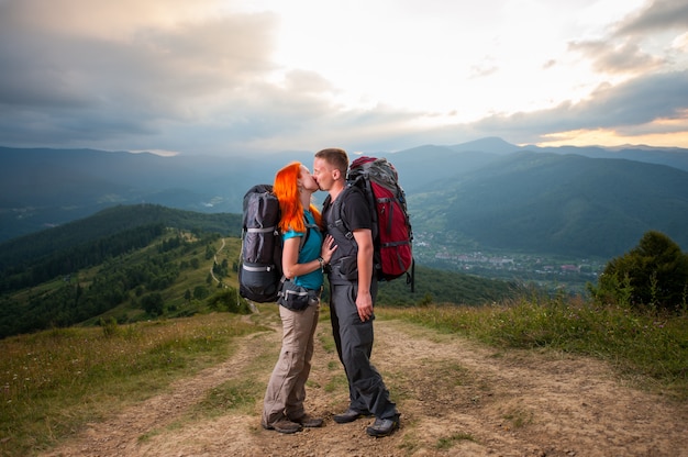 couple backpackers is kissing on the road in mountains
