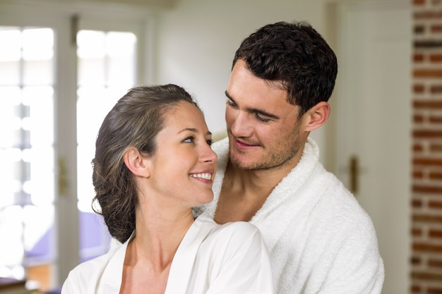 Couple in bathrobe smiling while embracing each other in kitchen