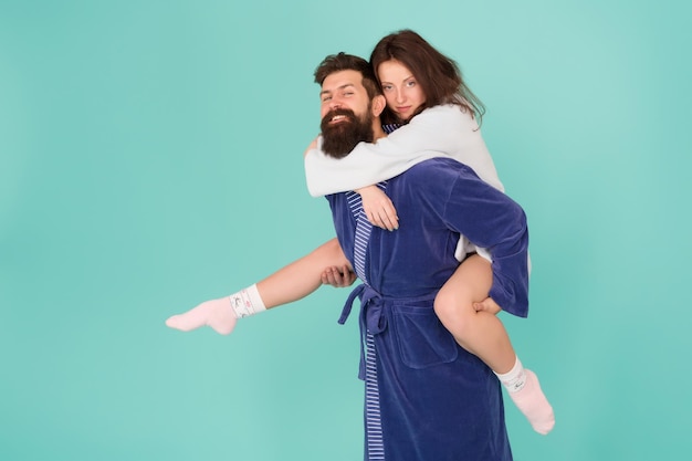 Photo couple in bathrobes having fun turquoise background lets stay at home and have fun they always have fun together close relationship handsome young man giving his girlfriend piggyback ride