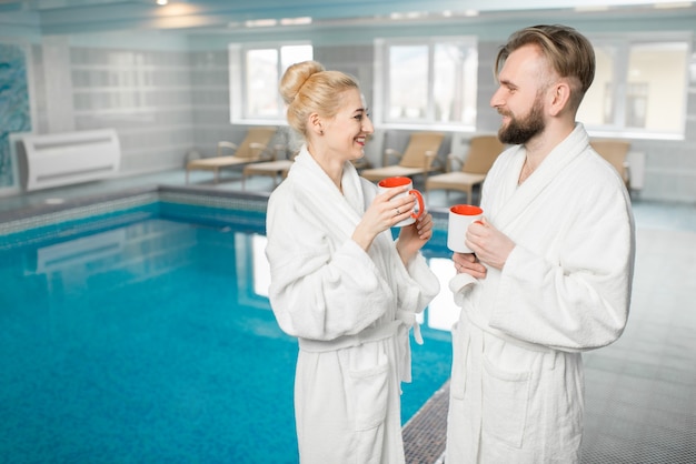 Couple in bathrobes relaxing in the spa near the basin during their holidays