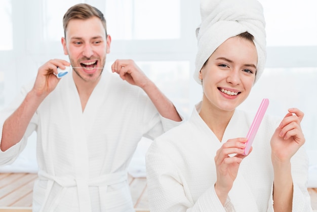 Couple in bathrobes using dental floss and nail file