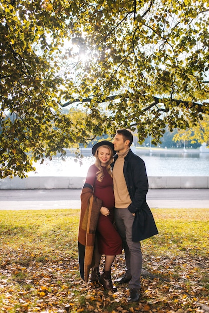 A couple of beautiful lovers spend time outdoors on the fall day pretty woman in a red dress and mod...