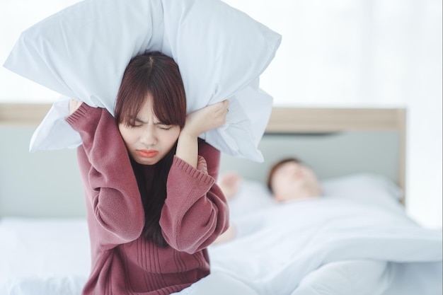 Couple in bed man sleeps and snores while woman is unable to
sleep closing her ears with big pillows