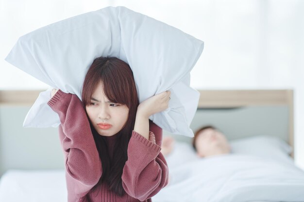 Coppia a letto l'uomo dorme e russa mentre la donna non riesce a dormire chiudendosi le orecchie con grandi cuscini