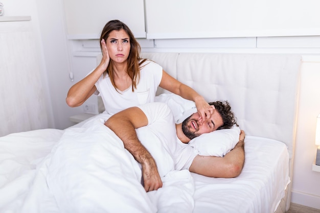 Couple in bed, man snoring and woman can't sleep. snoring man
and young woman. couple sleeping in bed. young girl can't sleep
because of her man's snoring holding his nose. snoring man
problem