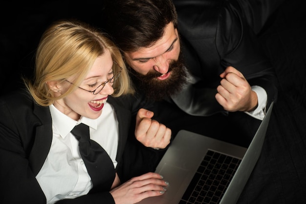 Couple being happy winning a bet in online sport gambling application on his notebook Excited Business people with laptop on black background isolated Young couple is working on laptop and smiling