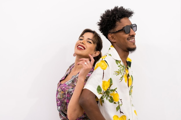 Couple of a black boy and a Caucasian girl on a white background, flowery shirts, smiling in a fashionable pose with their backs pressed together