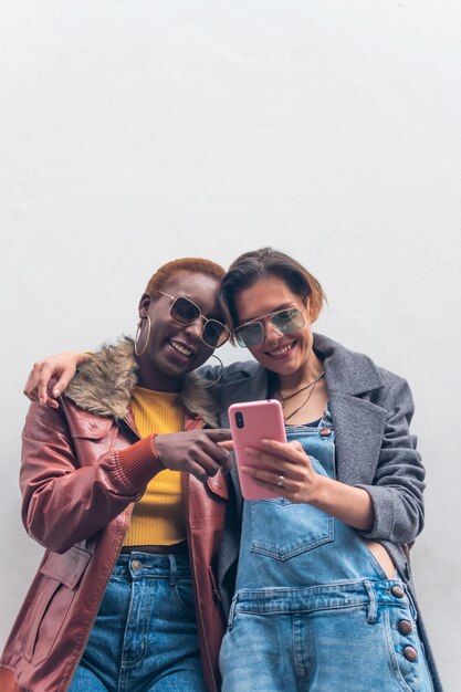 a couple of black and white women looking at a message on the smar phone in the street both smiling