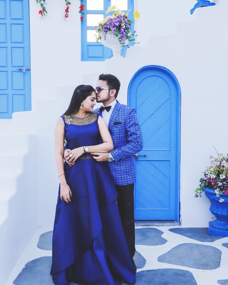 Couple in blue western outfits kissing forehead against santorini background