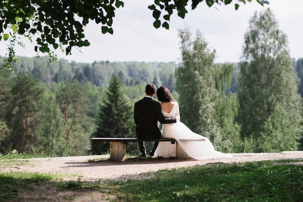 Couple bride and groom embrace sitting on a bench on a wedding day in summer in nature