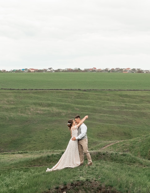 Couple of bride and groom near wedding arch embracing in green landscape