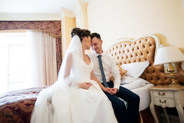 Couple of bride and groom posing indoors and kissing in bed