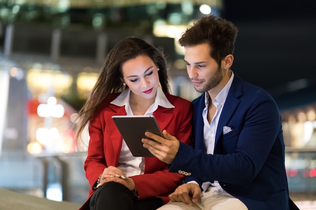 Couple of business people using a tablet outdoor at night in a modern city setting