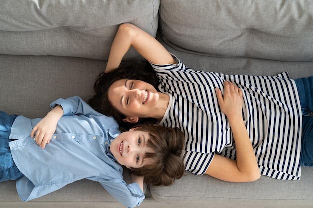 Couple of carefree mother and cute child lying resting on couch having fun looks together at camera