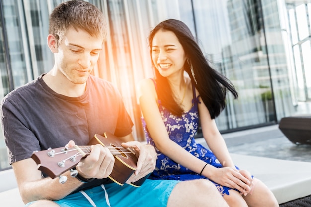 Coppia di amante indoeuropeo e asiatico giocare divertimento con la felicità e la posizione all'aperto canzone gioiosa e ukulele