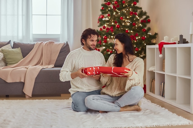 Couple celebration new year near christmas tree at home exchange presents in the gift boxes