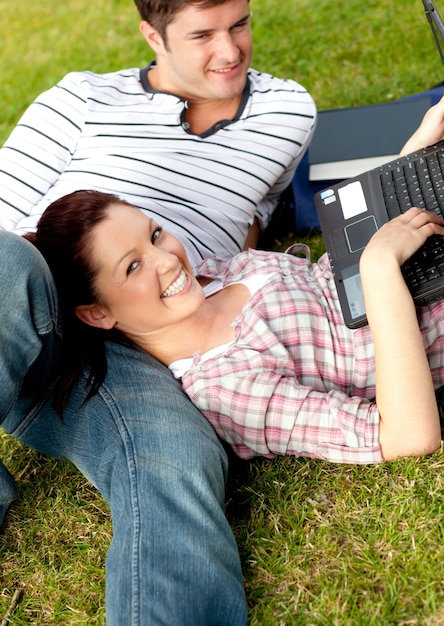 Пара веселых студентов, используя ноутбук, лежащих на траве