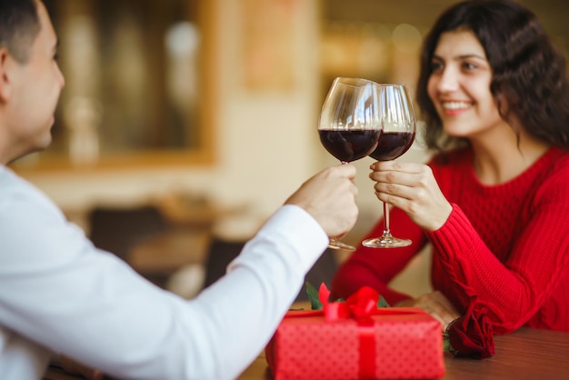 Couple clink glasses with red wine Lovers give each other gifts Lovely romantic dinner